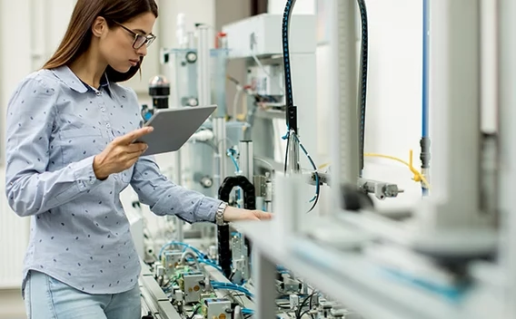 Woman wearing safety glasses holding a tablet monitoring an assembly line
